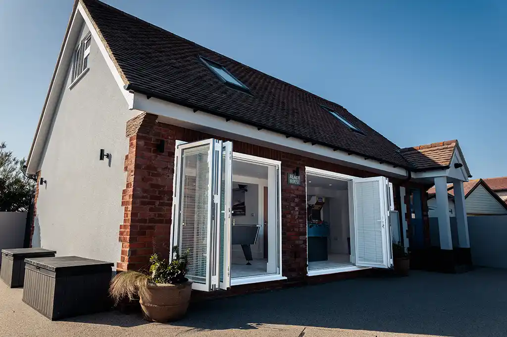 Exterior view of the brick annex at Selsey Beach House with open white bifold doors revealing a fully equipped games room.