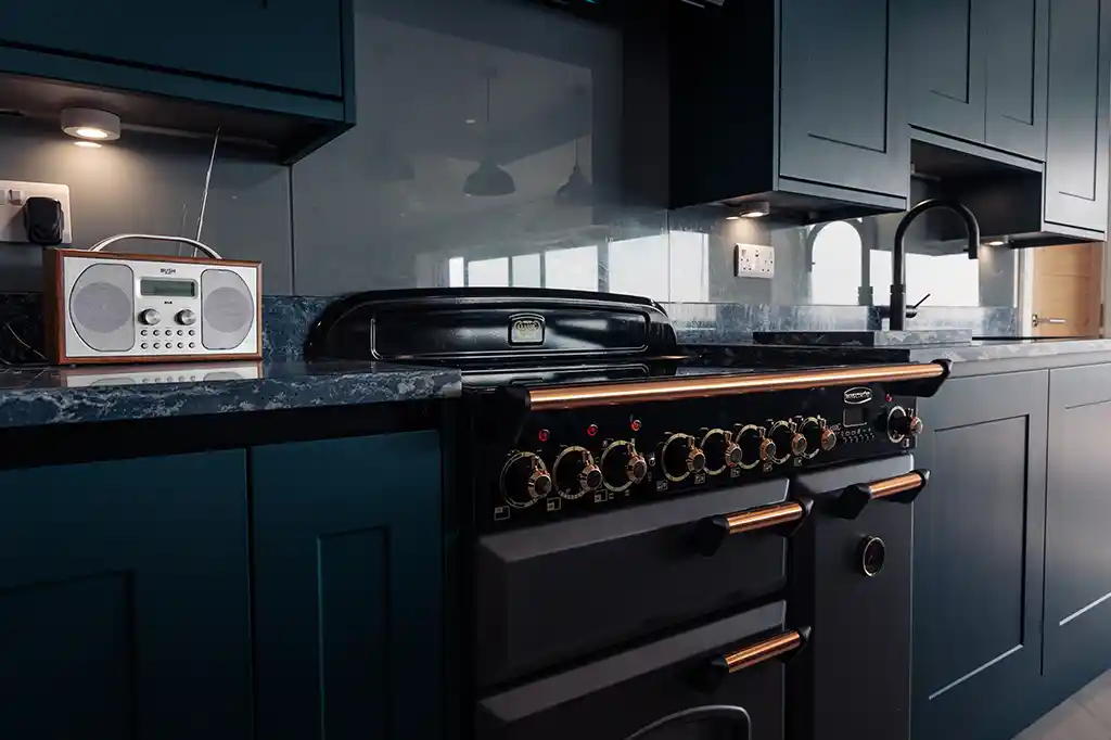 Fully equipped modern kitchen at Selsey Beach House featuring dark blue cabinetry, granite countertops, and a large black range cooker with copper details.
