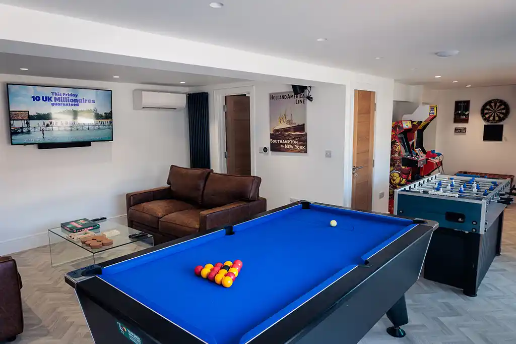 Fully equipped games room at Selsey Beach House featuring a blue pool table, table football, a retro arcade machine, and a lounge area.