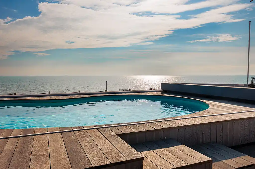 Private outdoor swimming pool with wooden decking and expansive ocean views at Selsey Beach House.