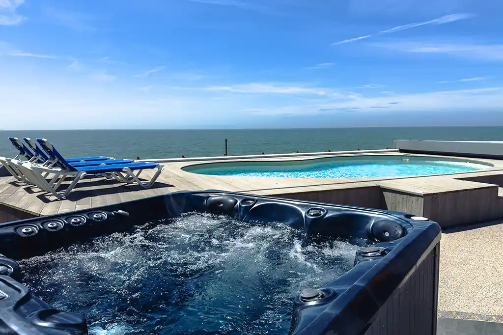 Outdoor hot tub and swimming pool at Selsey Beach House with sun loungers and panoramic ocean views.