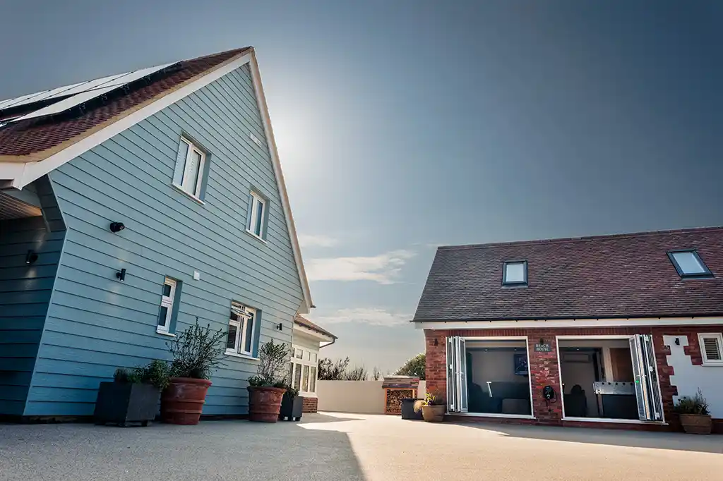 Front driveway of Selsey Beach House showing the blue weatherboarded main house and a brick annex with open bifold doors.