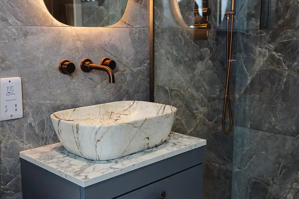 Close-up of the luxury bathroom vanity at Selsey Beach House featuring a marble vessel sink, wall-mounted bronze taps, and dark grey marble tiles.