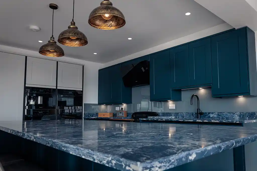 Spacious luxury kitchen at Selsey Beach House featuring a large granite island, dark blue cabinetry, and brass pendant lighting.