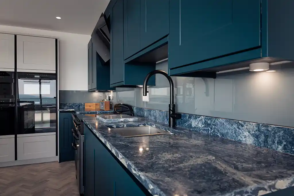 Modern kitchen at Selsey Beach House featuring dark blue cabinets, striking blue granite countertops, and a sleek black tap.