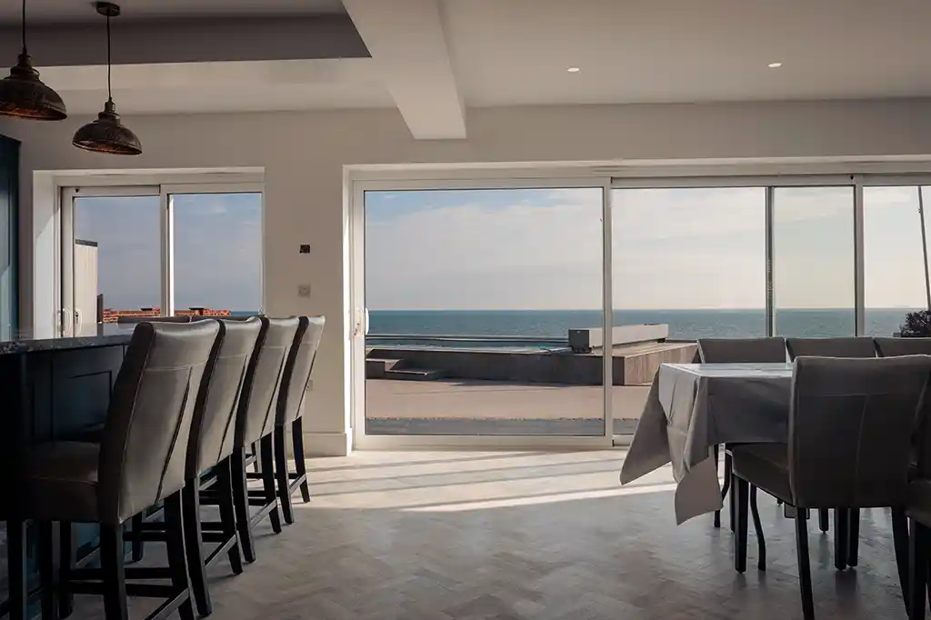 Open-plan kitchen and dining area at Selsey Beach House featuring large sliding glass doors with direct views of the outdoor pool and ocean.