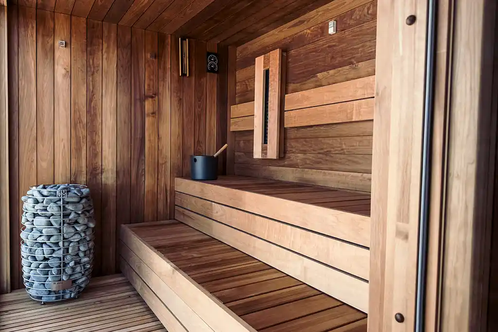 Interior view of the luxury wooden sauna at Selsey Beach House featuring tiered seating and a traditional stone heater.