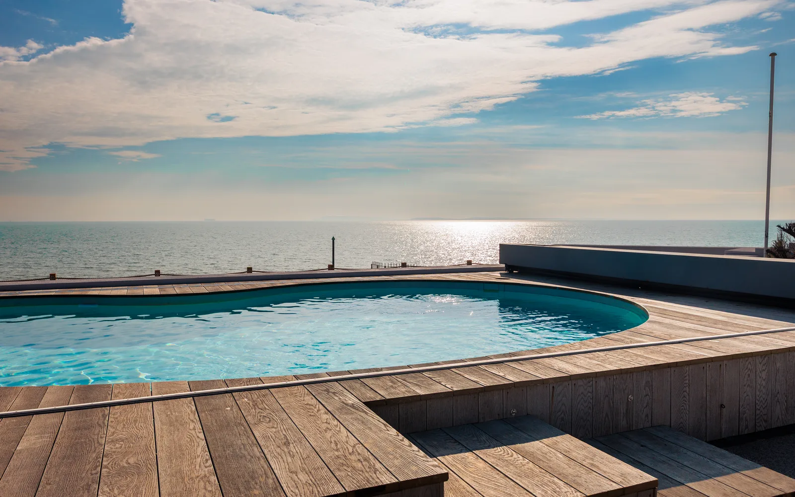 Luxurious Heated swimming pool with wooden decking overlooking the sea at Selsey Beach House, West Sussex
