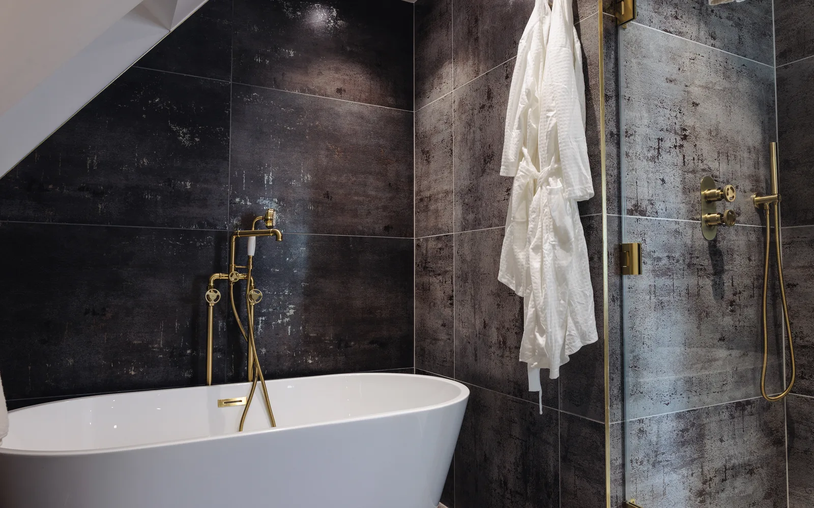 Luxury refurbished bathroom at Selsey Beach House with freestanding bath, dark tiling and brushed gold fittings